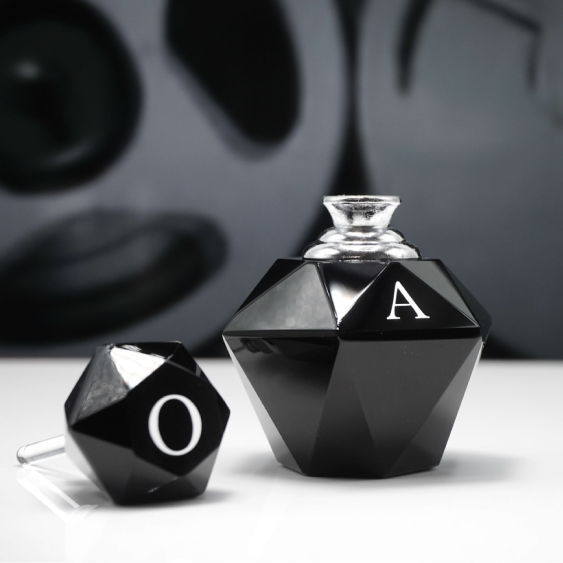 A black perfume bottle uncapped with the cap next to the bottle, on a white surface