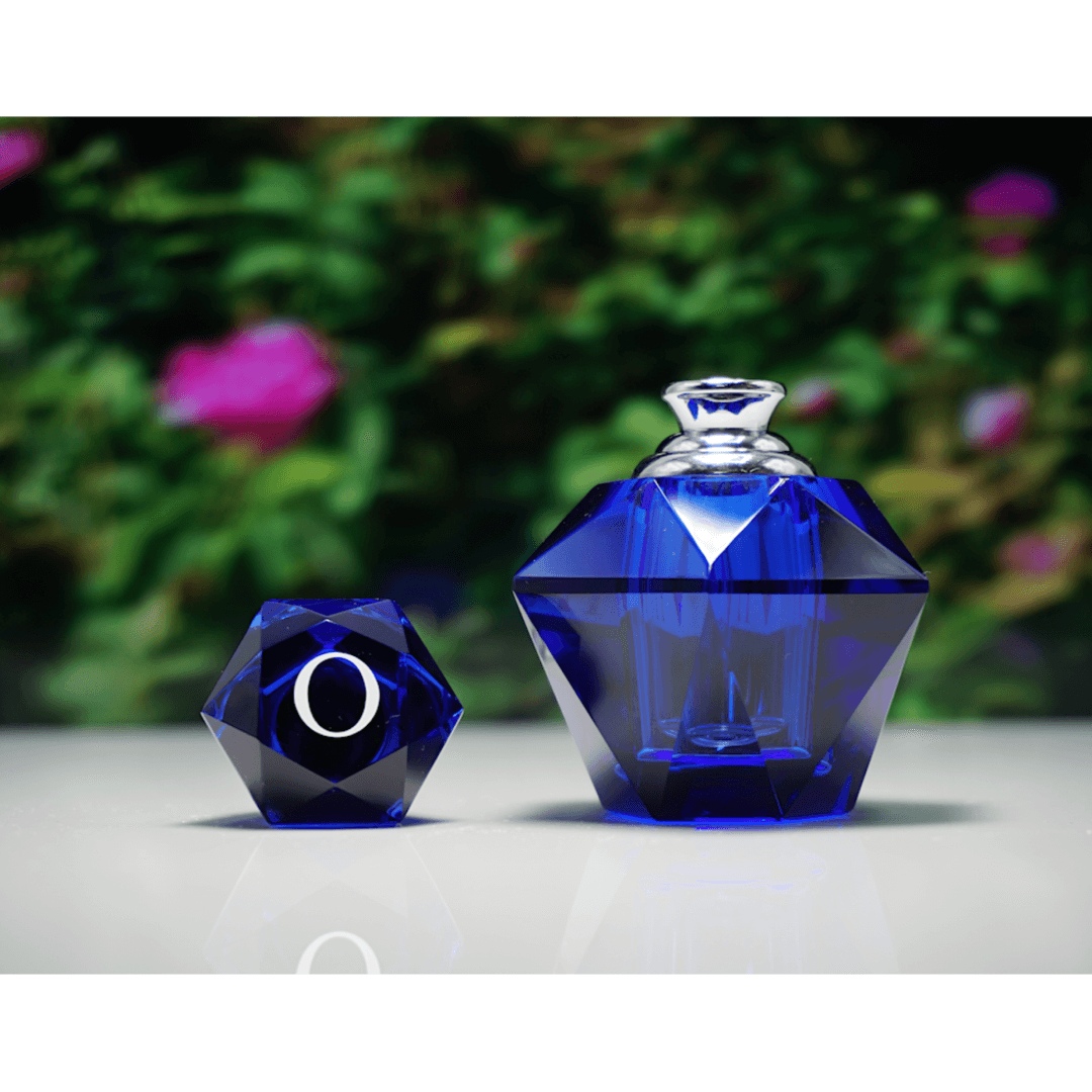 A blue perfume bottle uncapped with the cap next to the bottle, on a white surface